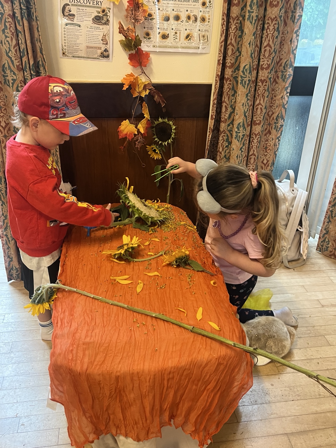 Two children exploring leaves and natural materials at an indoor autumn table