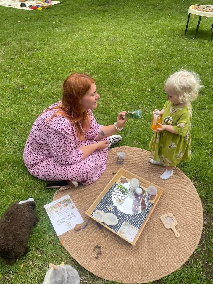 Jem sitting beside a young child and sharing sensory play on a woven mat