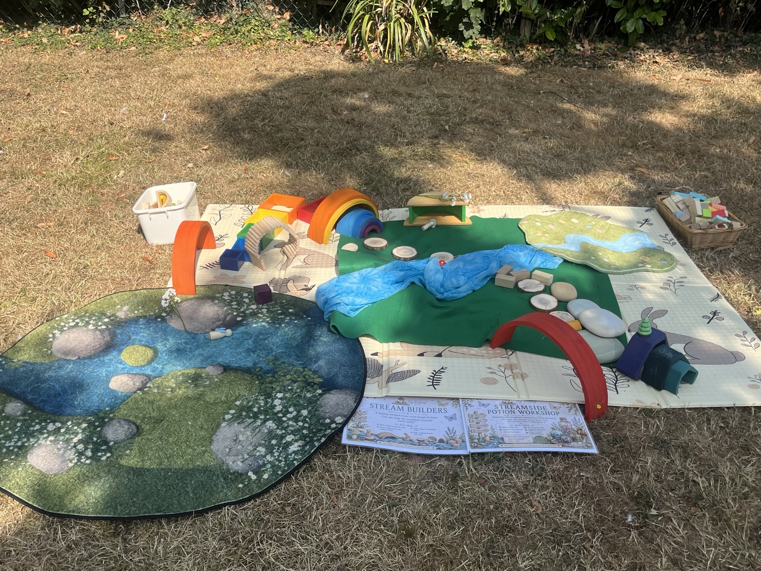 An invitation with a fabric river, wooden rainbows, stones and blocks laid out on a mat
